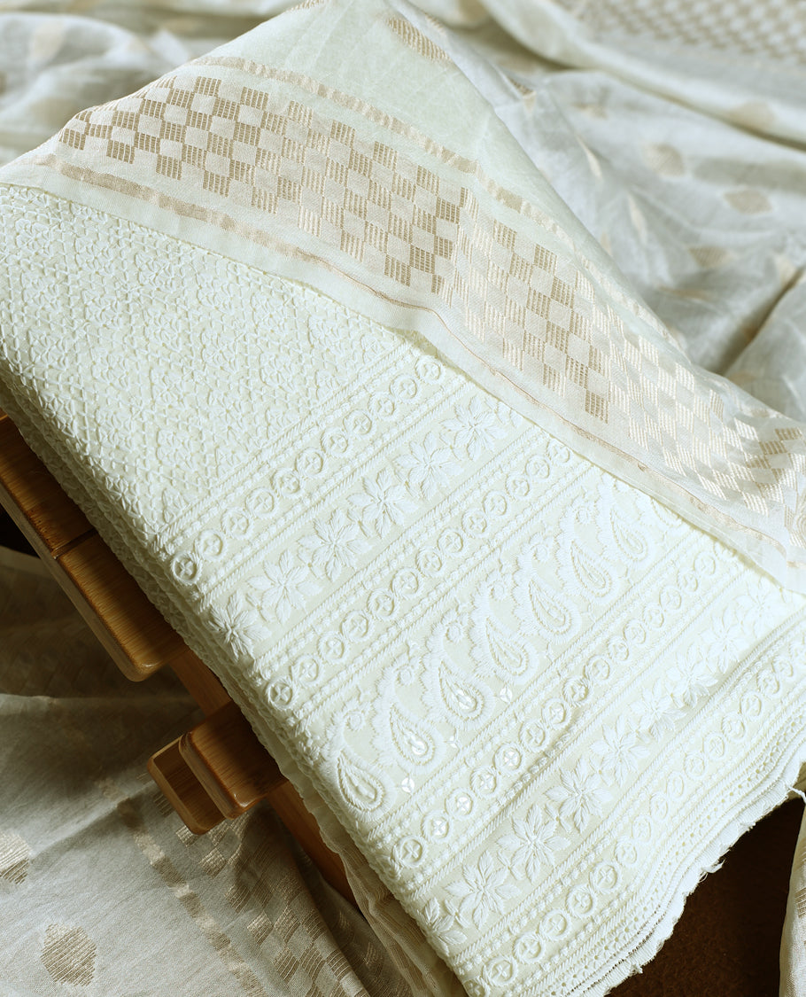 Off white colour churidhar material featuring delicate thread embroidery with paisley and floral motifs, paired with a plain bottom & Comes with a soft dupatta woven with subtle golden zari patterns.