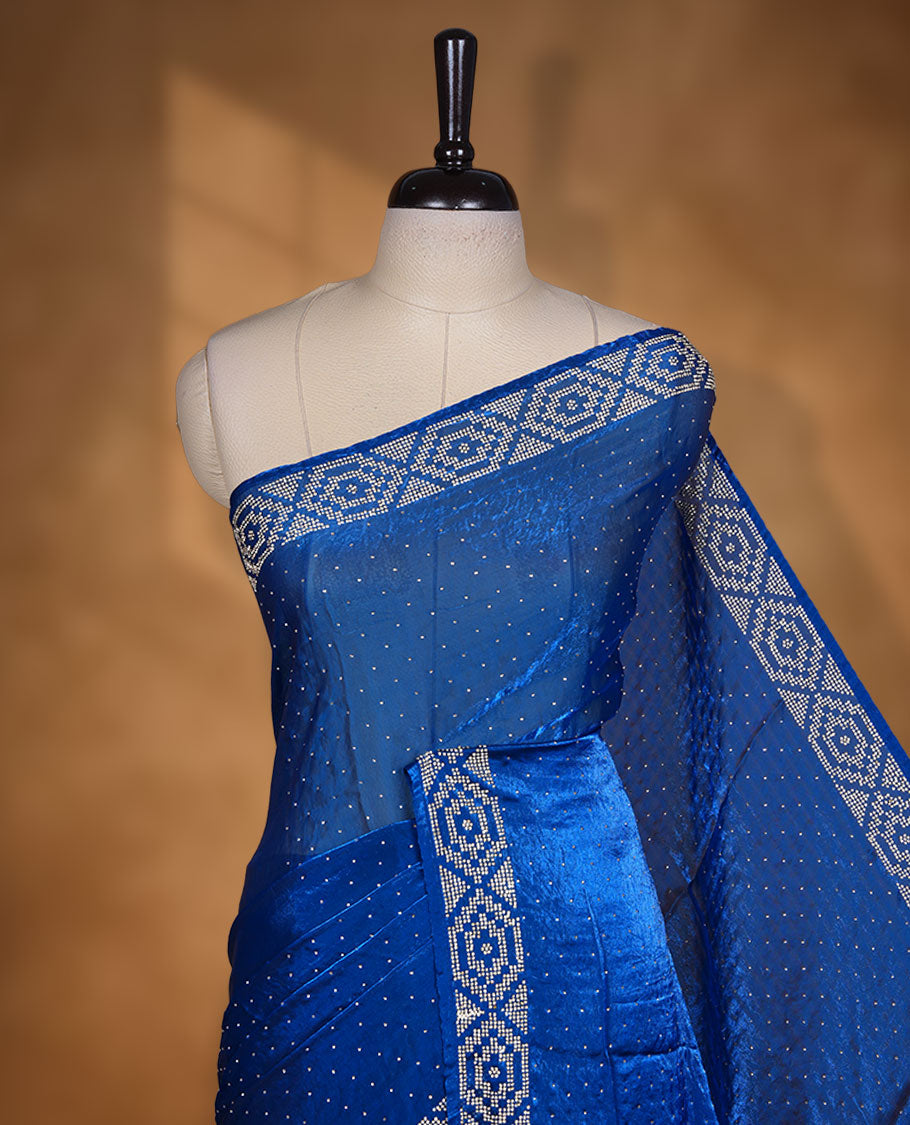 Royal Blue colour chiffon designer saree, featuring delicate scattered stone detailing all over the body, highlighted with intricate stone work and a heavy geometric stone pattern along the border and pallu, paired with a matching embellished blouse.a