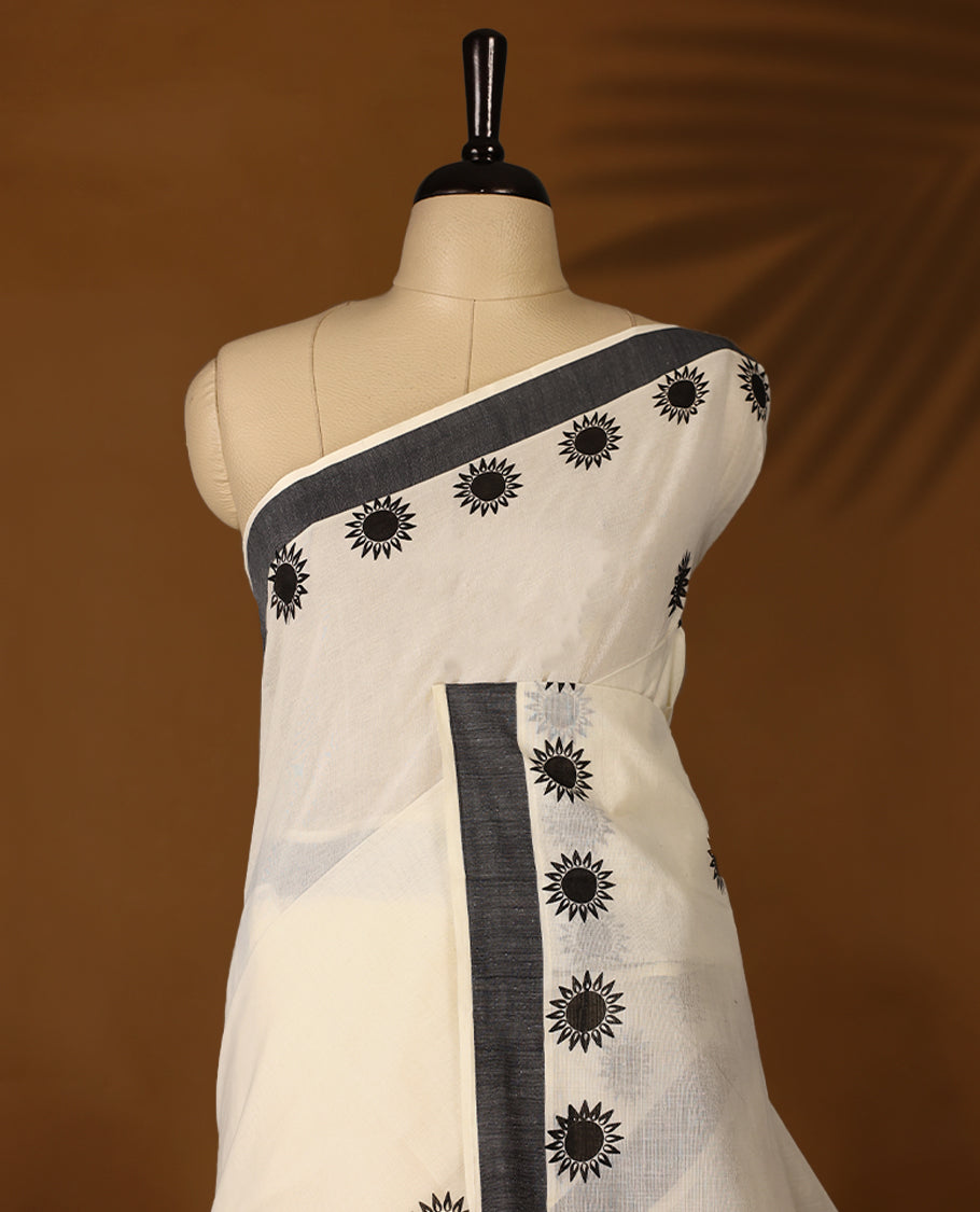 Elegant off white colour cotton Kerala saree featuring Plain body, Black colour border with Flower Block prints, Paired with matching blouse offering a classic and graceful look, paired with a matching blouse.