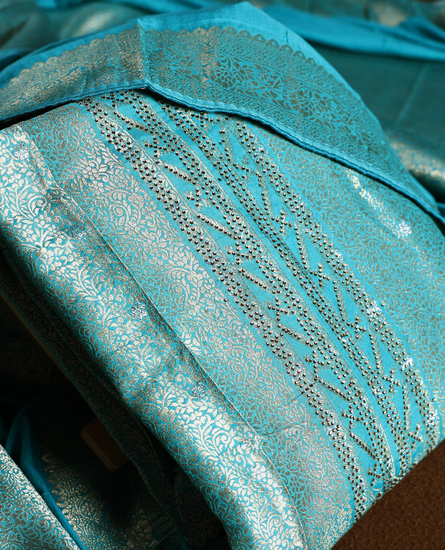 Turquoise blue colour churidhar material with elegant golden zari floral weaves and stone embellishments, paired with a plain matching bottom and dupatta.