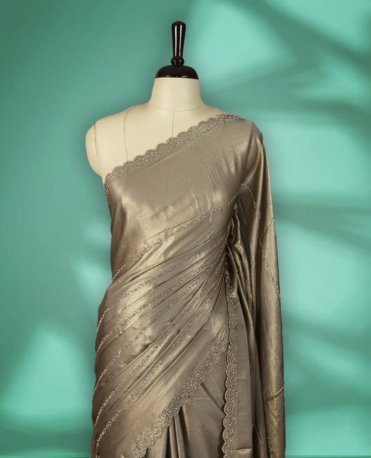 Khaki Beige colour shimmer fancy saree adorned with subtle horizontal Gold stone patterns on the body, paired with a delicate stone worked border, with matching blouse