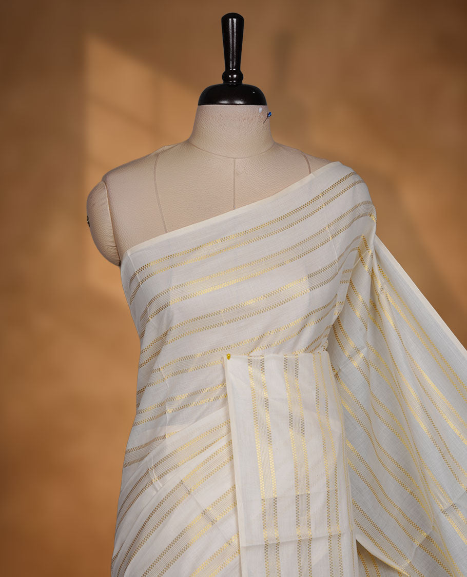 Off-white colour cotton Kerala saree featuring subtle gold zari stripe detailing across the body, finished with elegant green tassels on the pallu, and paired with a matching blouse.