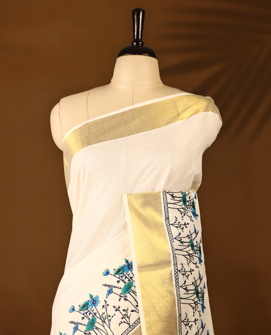 Light Gold colour Cotton Kerala saree featuring Plain body and a beautifully woven Gold Kasavu border with Heavy Blue and Green colour Floral embroidery work, paired with a matching blouse perfect for festive occasions.