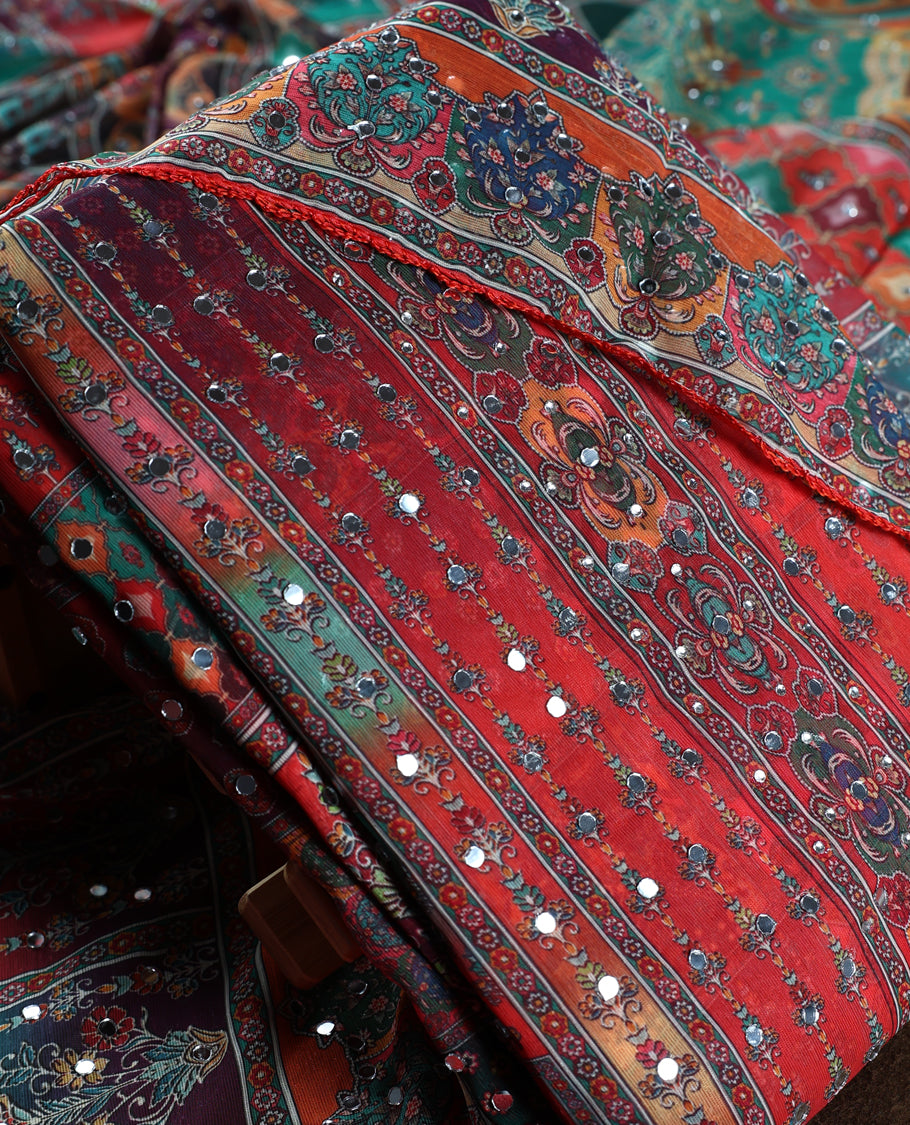 Red colour churidar material with rich floral and striped patterns enhanced by delicate mirror work, paired with a plain matching bottom and ornate dupatta.