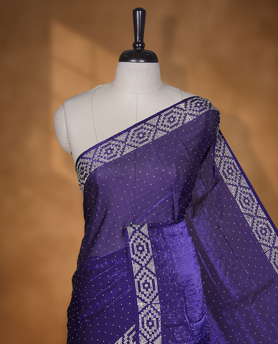 Dark violet colour chiffon designer saree, featuring delicate scattered stone detailing all over the body, highlighted with intricate stone work and a heavy geometric stone pattern along the border and pallu, paired with a matching embellished blouse.a