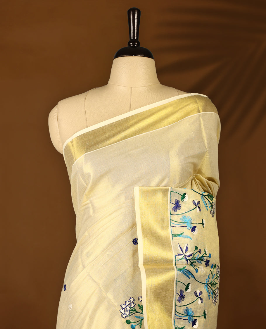 Light Gold colour Tissue Kerala saree featuring Blue and white Colour Floral thread work on body and a beautifully woven Gold Kasavu border, paired with a matching blouse perfect for festive occasions.