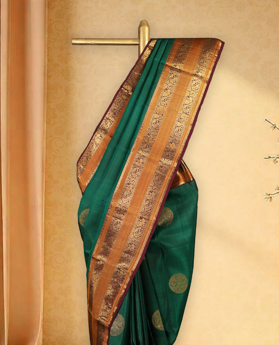 Bottle green pure Kancheepuram saree with gold zari Mayoora Chakra and diamond motifs on the body, contrast brown Kalakshetra border, grand pallu, and matching blouse.