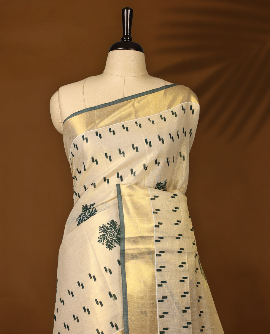 Elegant off white tissue Kerala saree with green woven motifs and floral buttas, paired with a rich golden zari border and pallu paired with matching blouse.