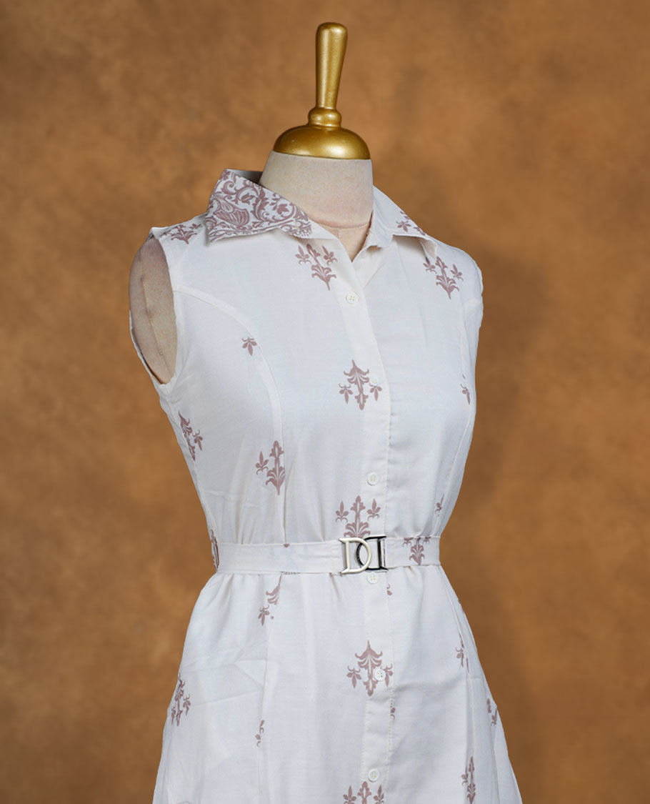White sleeveless shirt dress with subtle mauve ethnic motifs, front button placket, matching waist belt with metal buckle, and ornate border print at the hem.