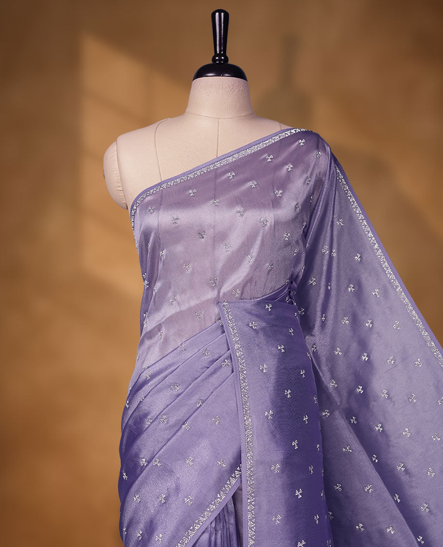 Lavender colour net shimmer fancy saree adorned with scattered white stone buttas all over the body, paired with a delicate stone worked border and matching blouse featuring floral vine stone embroidery