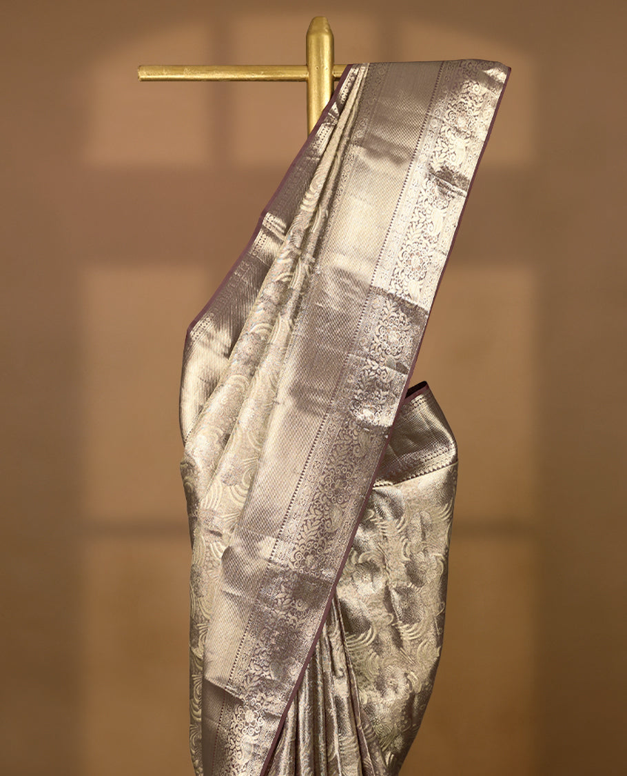 Pastel brown Colour Kancheepuram tissue silk saree adorned with intricate silver and pastel brown Zari floral motifs on the body, gracefully complemented by a traditional mango and floral design border, and paired with a matching blouse.
