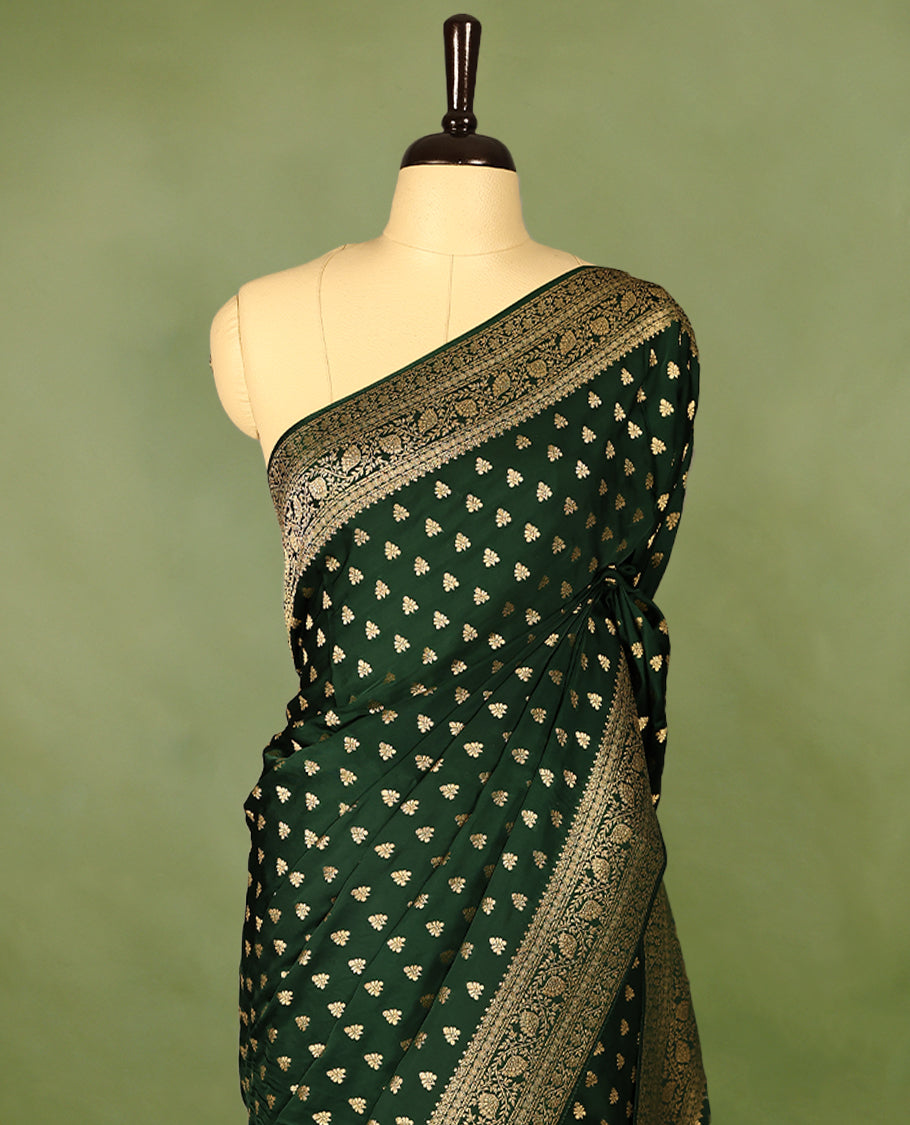 Bottle green semi-Banaras satin crepe saree featuring traditional closely woven buttas on the body, complemented by an antique-style border and a matching self-coloured blouse.