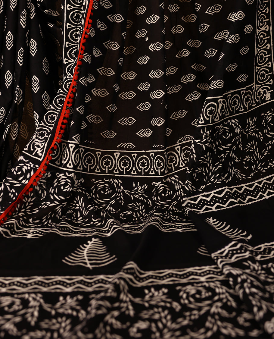 Black cotton saree features intricate white handblock prints, a beautifully detailed border with red piping and Self Coloured Blouse