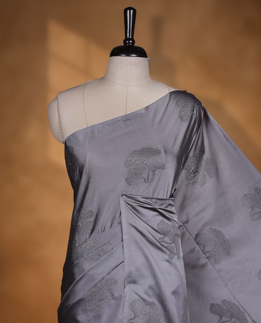 Silver gray colour semi soft silk saree adorned with delicate woven floral kodi motifs on the body, complemented by a Self colour woven pallu with intricate detailing and tassel accents without border & Comes with a matching blouse piece.