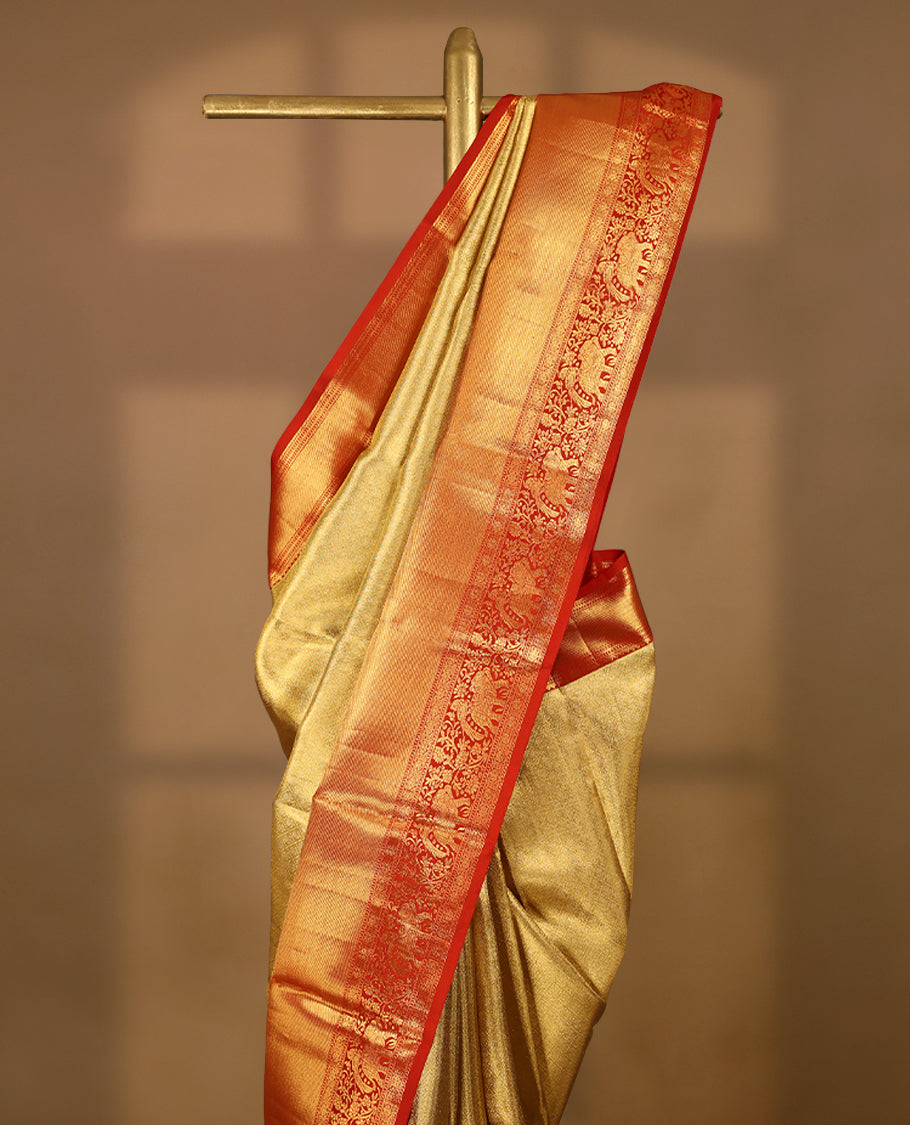 Gold Colour Kancheepuram tissue silk saree featuring an intricately woven antique zari jacquard design on the body, elegantly complemented by a bright red traditional border with elephant, bird, and Rudraksham motifs, and paired with a matching blouse.
