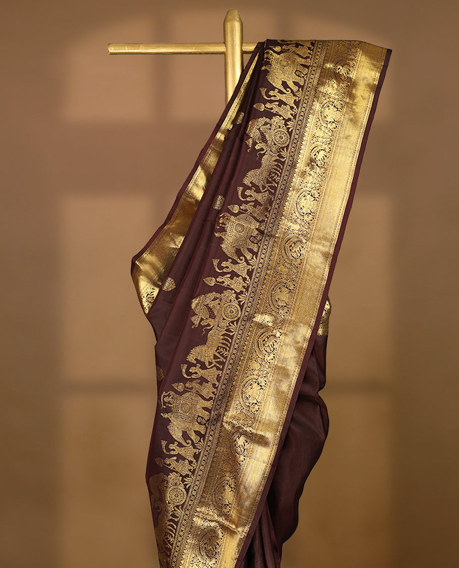 Dark brown colour pure traditional Kancheepuram silk saree adorned with golden Floral motifs on the body, featuring an exquisite antique zari border, paired with a contrasting blouse.