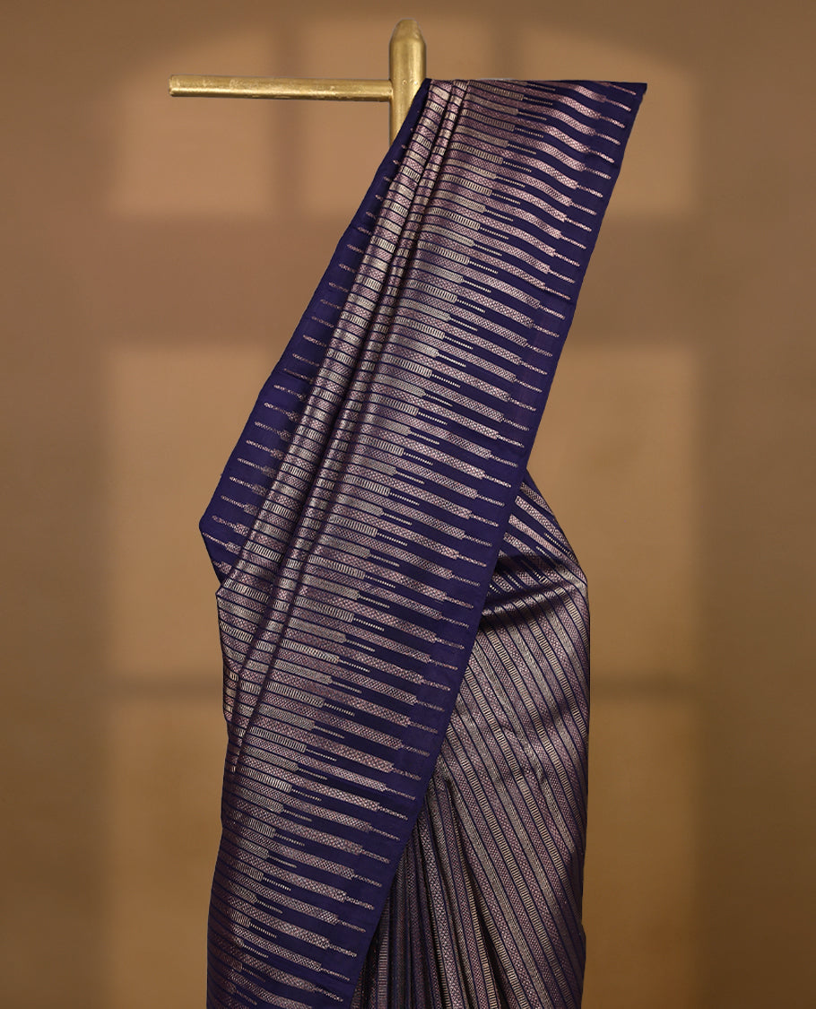 Ink purple colour Kancheepuram designer saree adorned with distinctive vertical zari lines featuring intricate arrowhead and herringbone motifs on the body, designed without a border, and paired with a matching blouse.