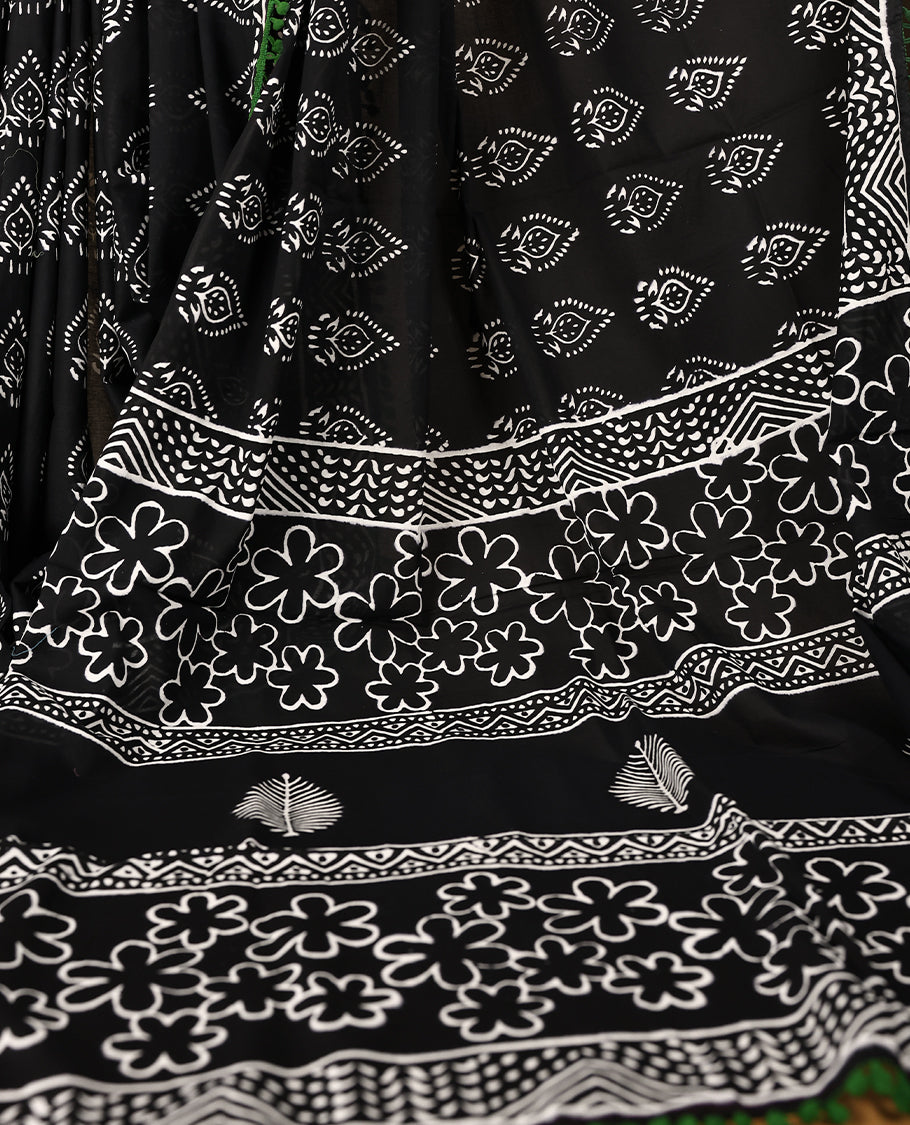 Black cotton saree features intricate white handblock prints, a beautifully detailed border with Green piping and Self Coloured Blouse