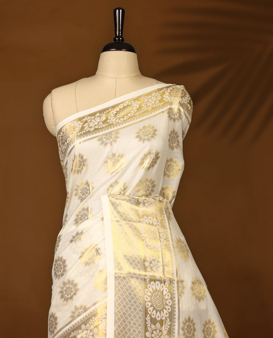 Elegant off white colour soft cotton Kerala saree adorned with golden floral motifs all over, accentuated by an ornate golden pallu with tassels, and a matching blouse, making it a perfect choice for traditional and festive celebrations.