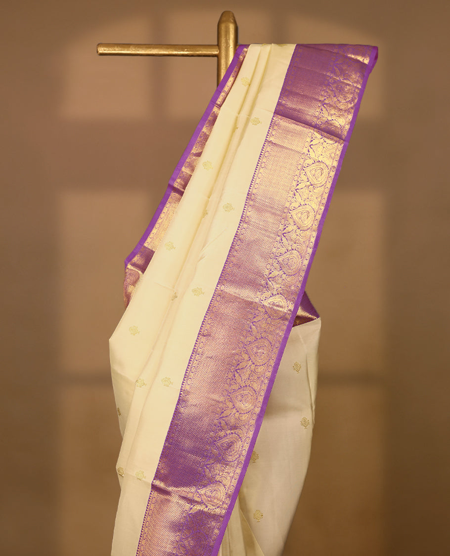 Cream Colour traditional Kancheepuram silk saree adorned with golden motifs on the body, featuring a Light Purple traditional border with Rudraksham and mango designs, paired with a matching blouse.