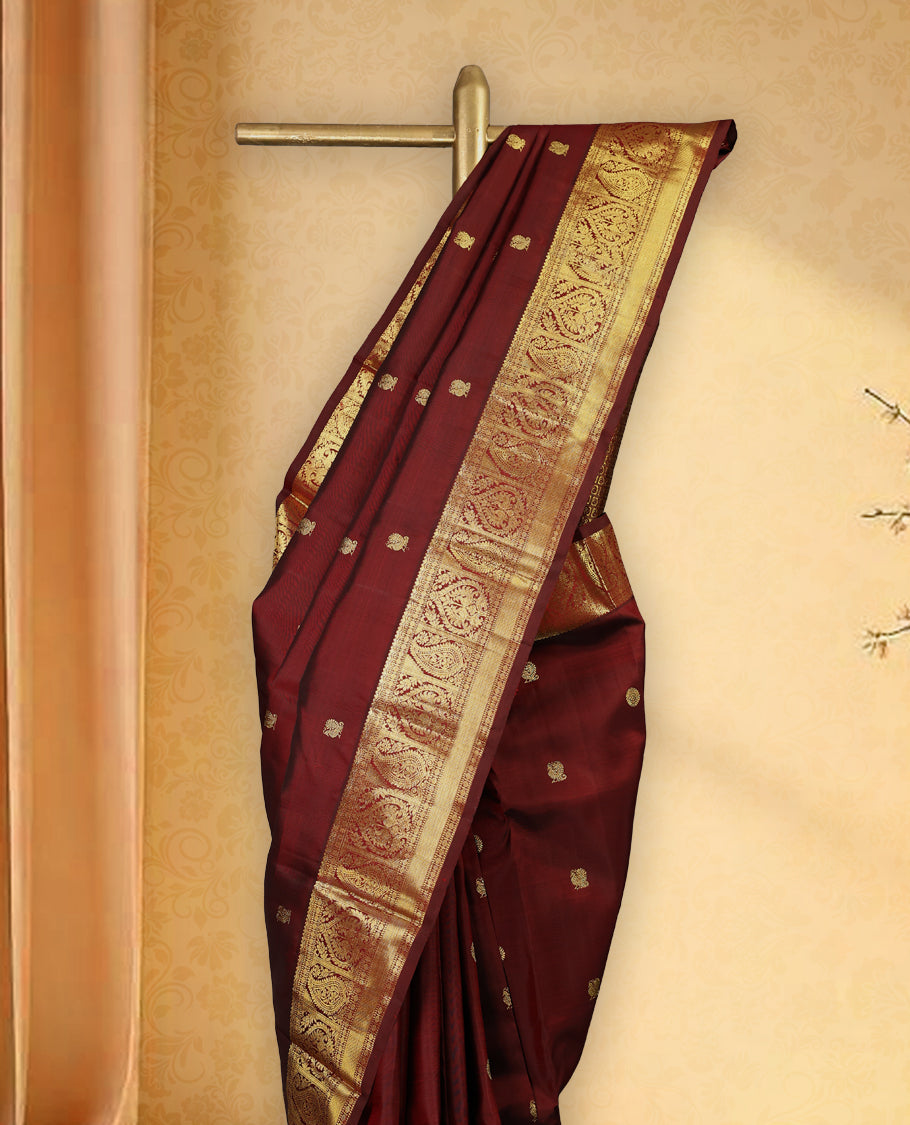 Deep maroon colour pure Kancheepuram traditional saree featuring gold zari Mayoora Chakra motifs across the body, enhanced with a classic traditional border with Peacock and mango design and a grand pallu with Mango designs, paired with a matching blouse.