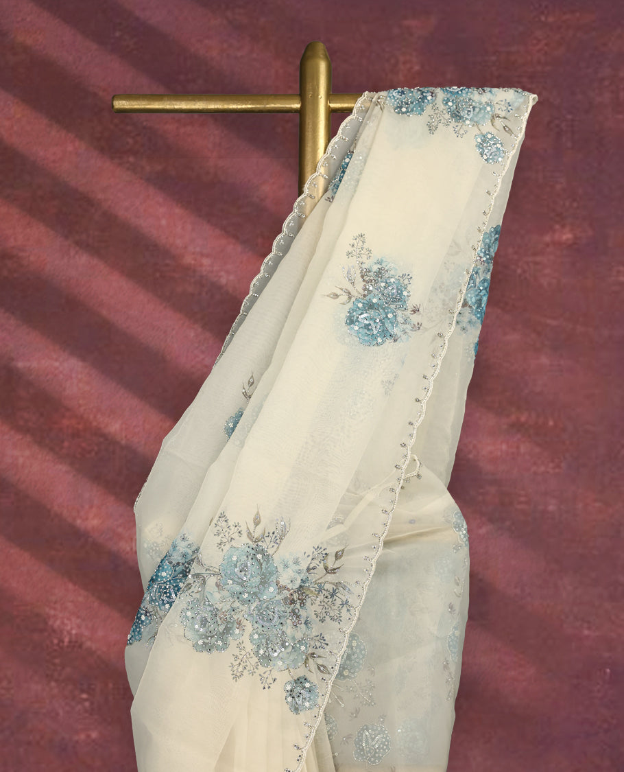 White colour pure organza saree featuring blue Colour floral prints with intricate bead and sequin work across the body, adorned with a matching embellished border, complemented by a worked pallu and paired with a heavily worked matching blouse.