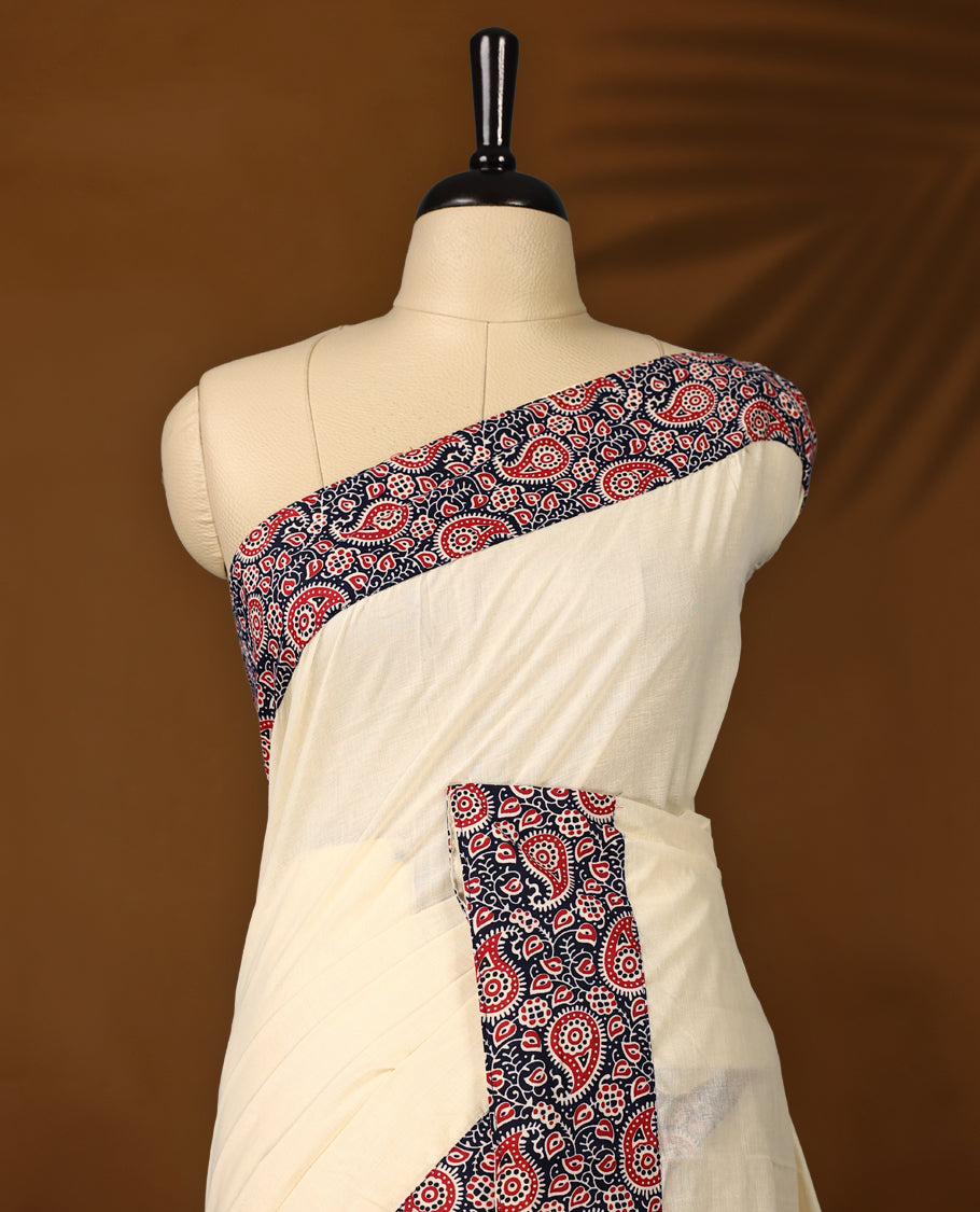 Off white colour cotton Kerala saree featuring a navy blue border with red and white paisley prints, paired with a matching printed blouse for a traditional yet vibrant look