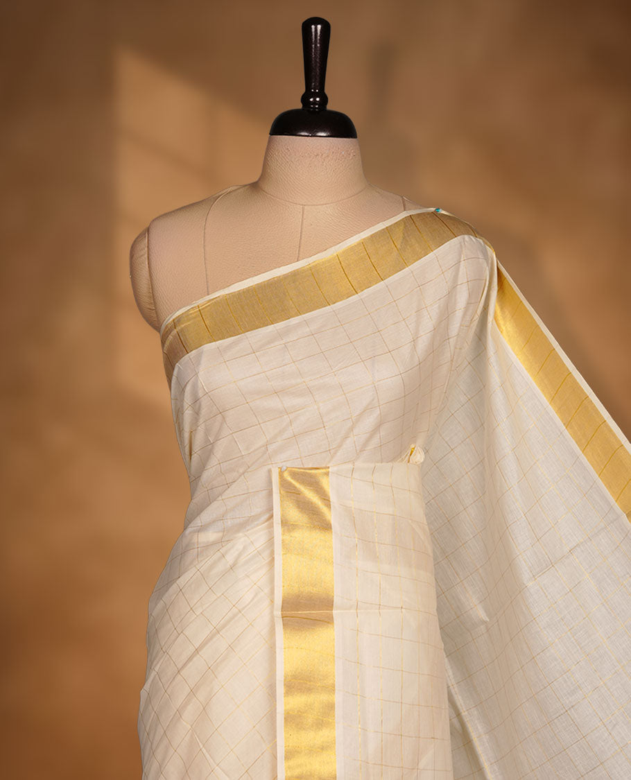 Off-white colour cotton Kerala saree featuring a classic gold kasavu border, highlighted by subtle woven check patterns across the body and pallu, and paired with a matching blouse.