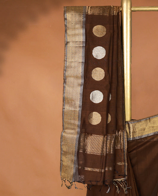 Brown colour Maheshwari Cotton saree featuring Antique Zari bindi Patterns across the entire body, complemented by a traditional Gold Zari border & Pallu, with a matching blouse.