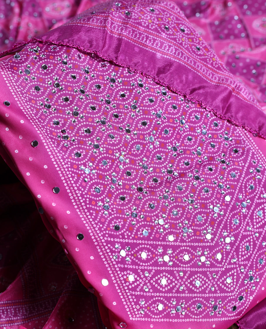 Magenta colour churidhar material adorned with intricate bandhani patterns and sparkling mirror work, paired with a plain matching bottom and elegant dupatta, perfect for festive gatherings and traditional celebrations.