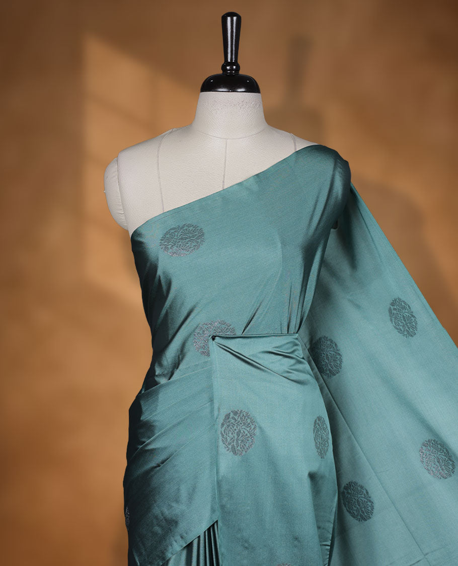 Pine green colour semi soft silk saree adorned with delicate woven floral motifs on the body, complemented by a contrast dusty pink colour woven pallu with intricate detailing and tassel accents without border & Comes with a matching blouse piece.