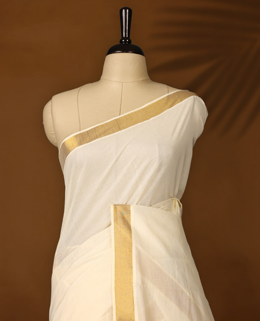 Traditional off white colour cotton Kerala saree with golden zari border and temple motif pallu, Accented with small golden buttas and paired with a matching blouse, Ideal for festive and cultural events.