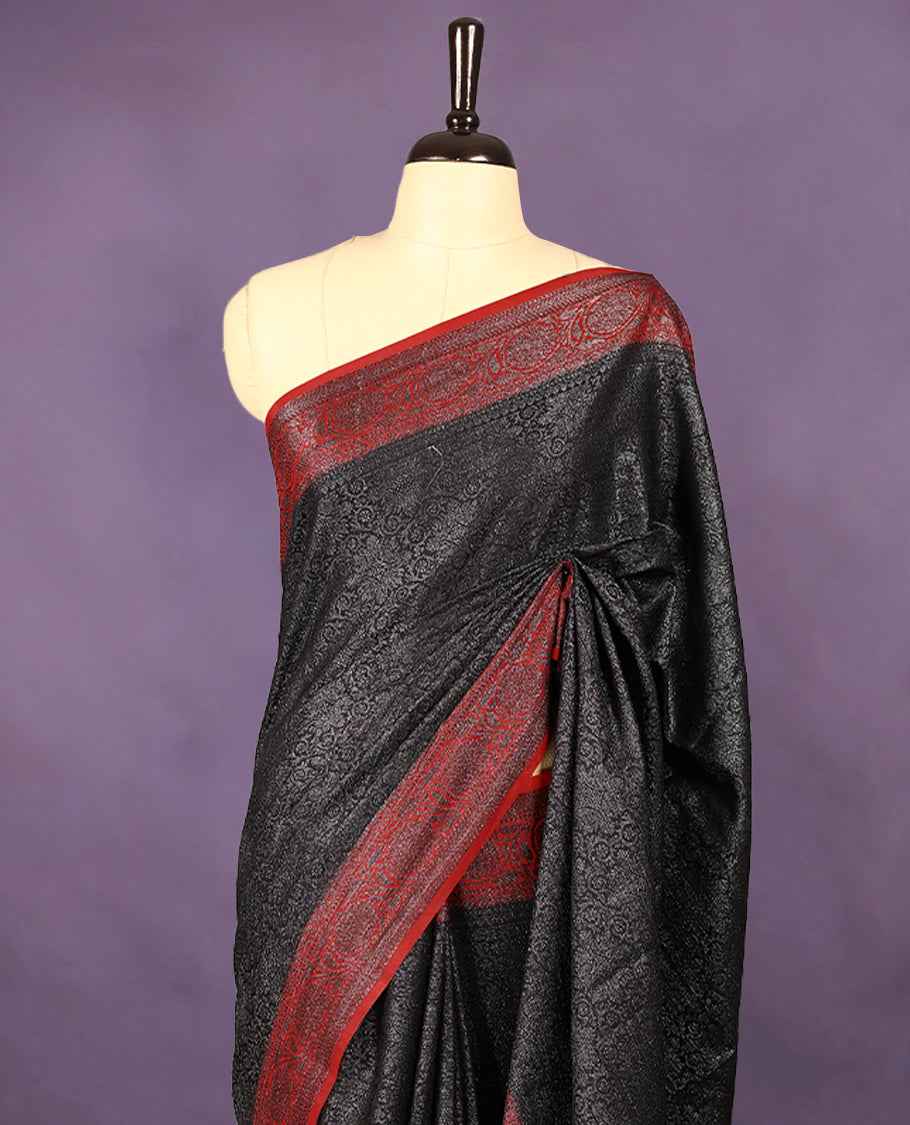 Black colour semi Banaras Katan saree featuring an antique zari jacquard body, complemented by a contrasting traditional border with a floral kodi design, paired with a matching blouse.