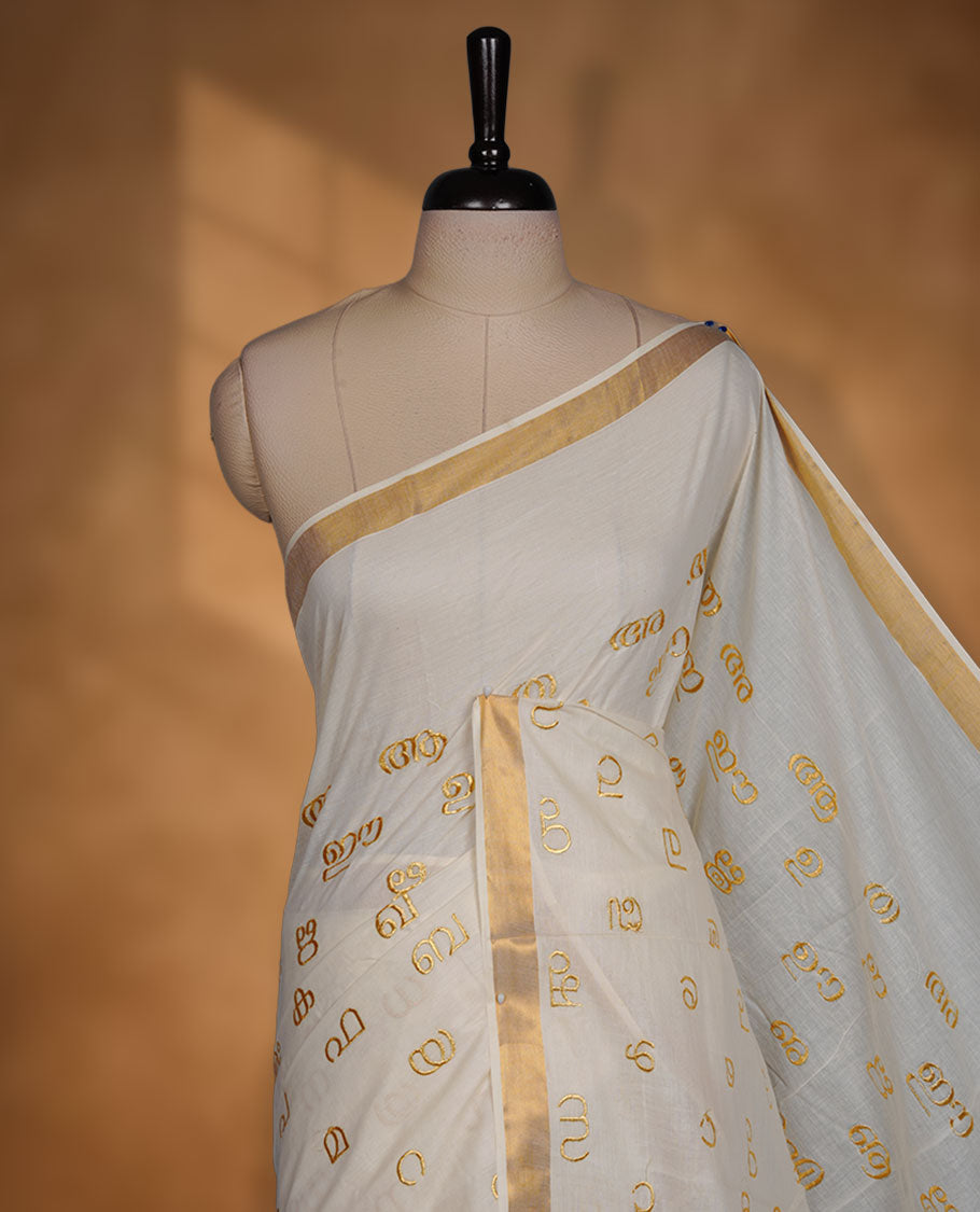Off-white colour cotton Kerala saree, featuring a classic gold kasavu border and delicate gold-toned Malayalam script motifs woven across the body and pallu. paired with a matching blouse