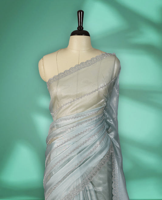 Icy blue colour net shimmer fancy saree adorned with subtle horizontal White stone patterns on the body, paired with a delicate stone worked border, with matching blouse
