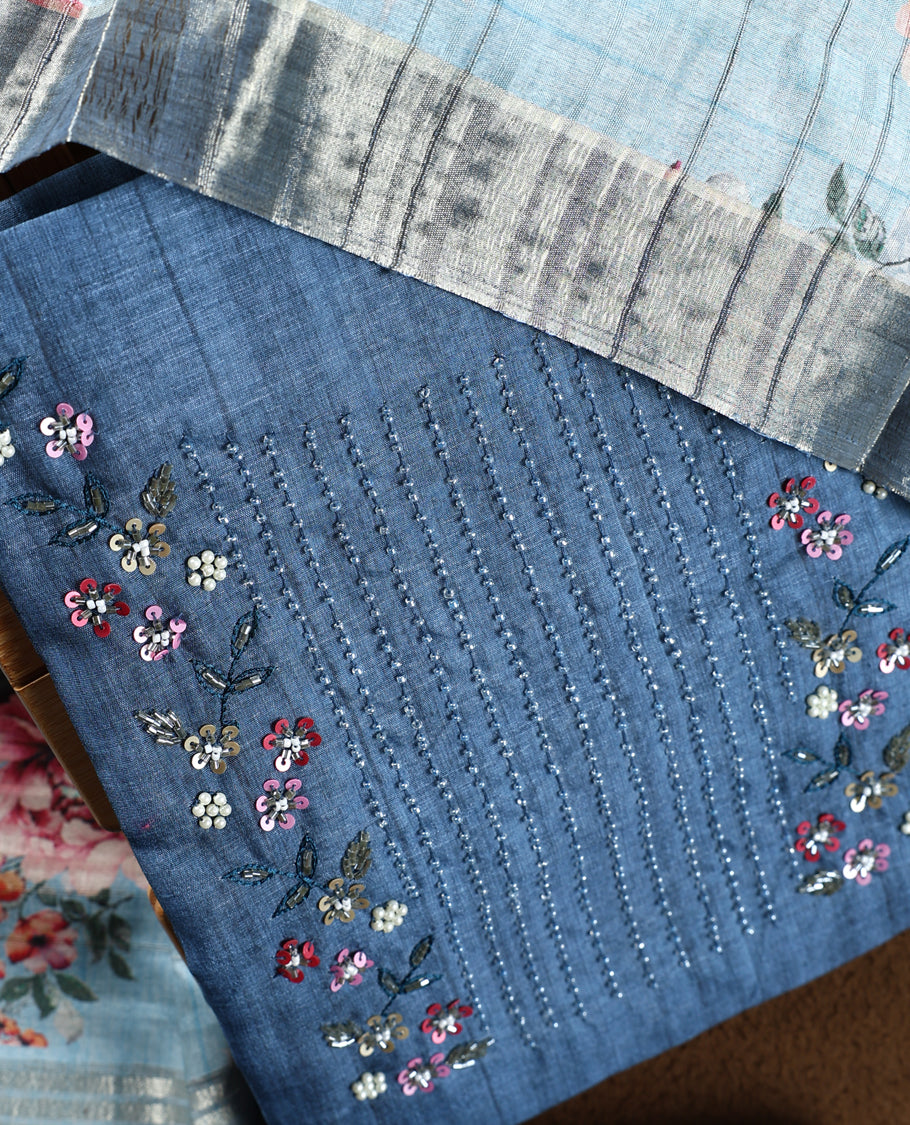 Dark pastel blue colour churidhar material adorned with floral embroidery and sewn glass beads on the yoke, paired with a plain blue bottom and a beige dupatta featuring floral prints.