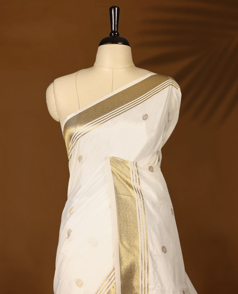 Elegant white colour sotf Tussar Kerala saree featuring Flower motifs on body, Gold kasavu border, Rich Pallu, Paired with matching blouse offering a classic and graceful look
