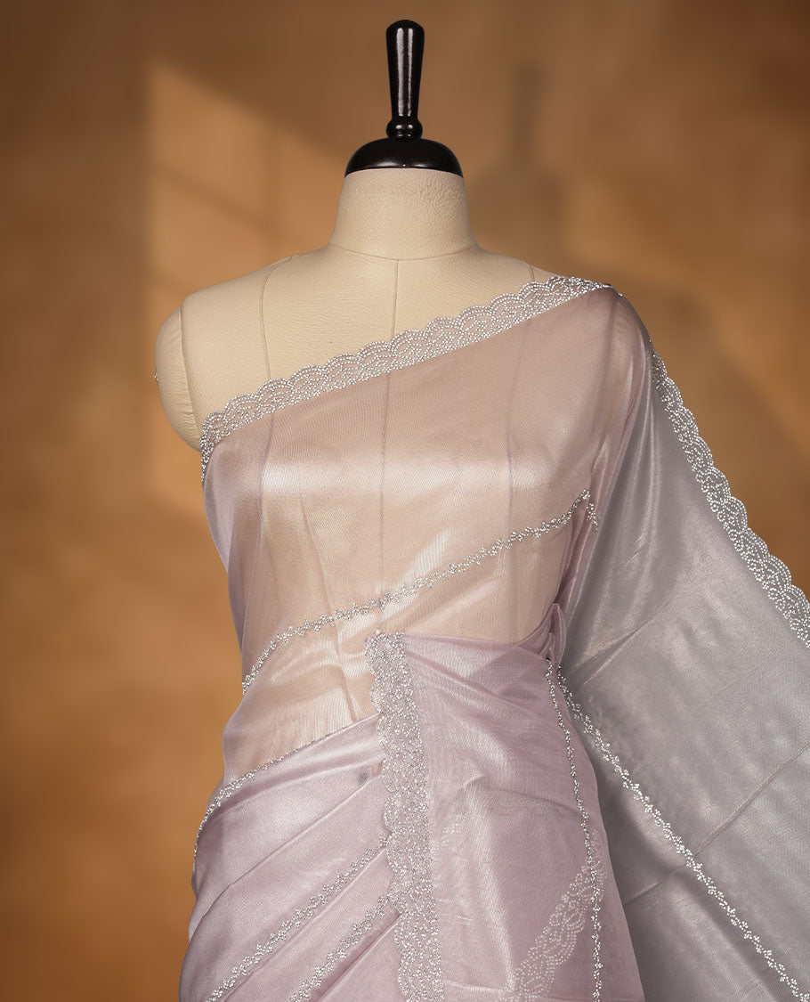 Light lavender colour net shimmer fancy saree adorned with scattered white stone buttas all over the body, paired with a delicate stone worked border and matching blouse.