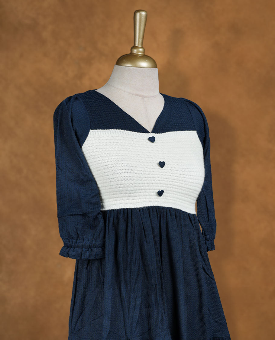 Navy blue knee-length tiered dress with V-neckline, contrast white textured yoke with button detail, and three-quarter puff sleeves.