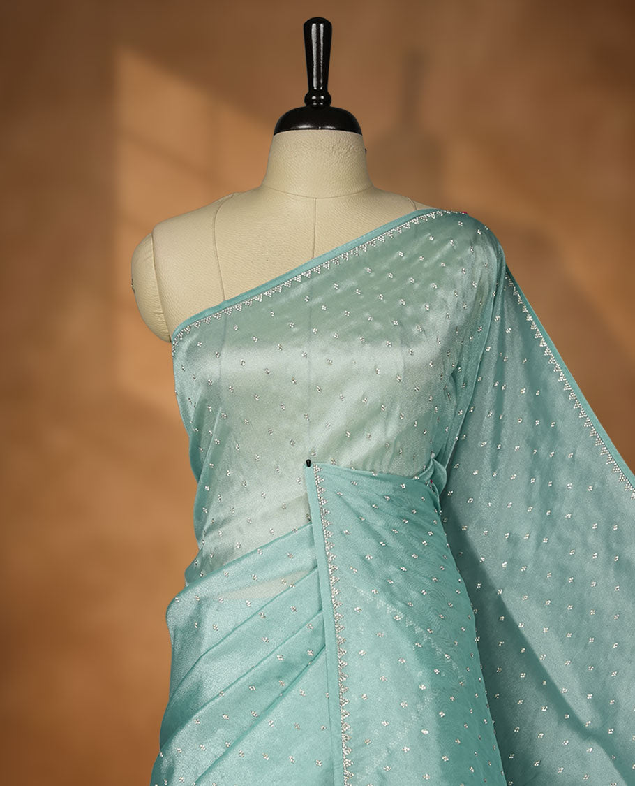 Pastel teal colour net shimmer fancy saree adorned with scattered white stone buttas all over the body, paired with a delicate stone worked border and matching blouse.