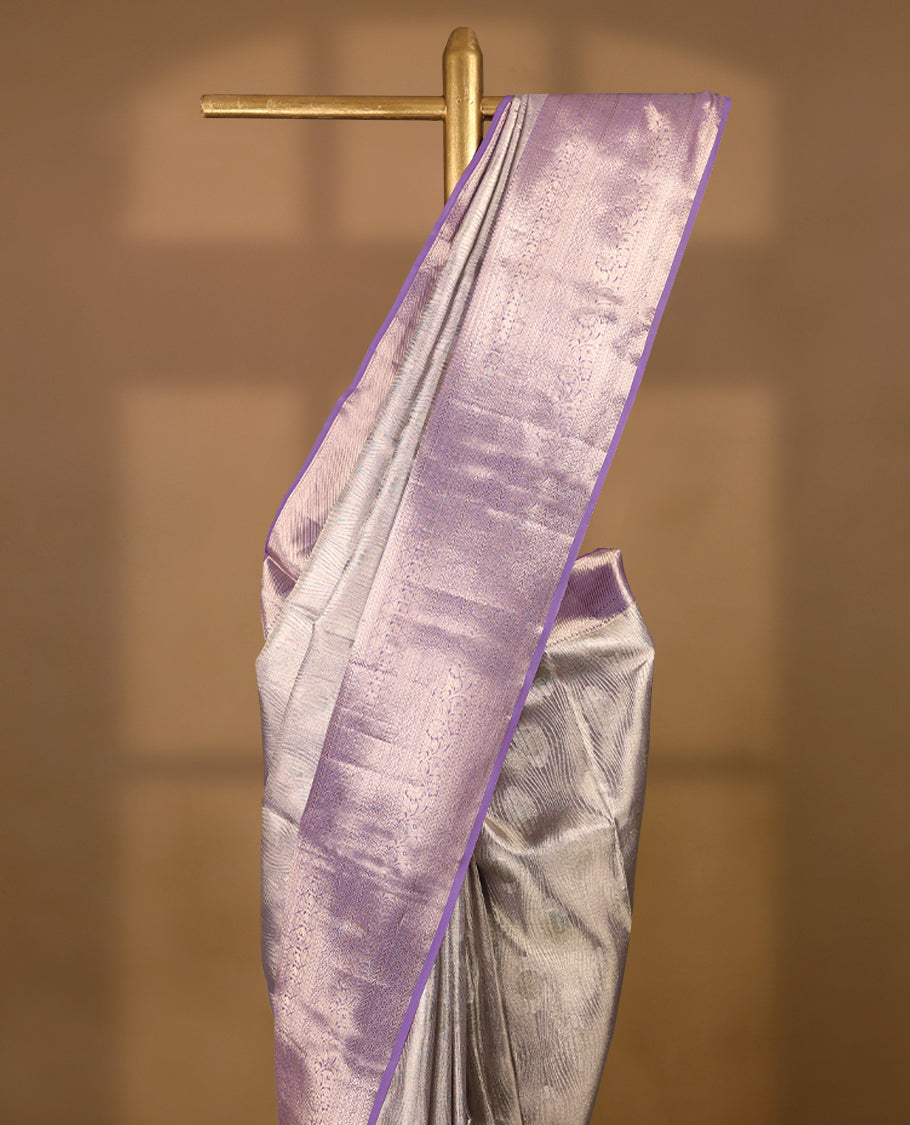 Pastel lavender Colour Kancheepuram tissue silk saree embellished with intricate silver zari work on the body, elegantly enhanced by a lavender traditional Chakkram and floral kodi design border, and paired with a matching blouse.
