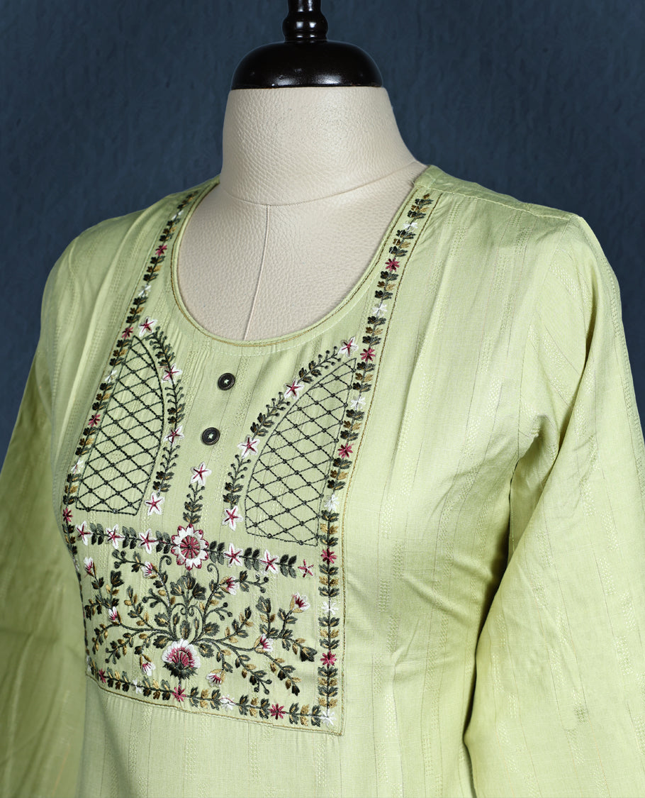 Light green colour kurti with subtle vertical self stripes, highlighted by an intricately embroidered yoke in floral and geometric patterns, featuring a round neckline with button accents and three quarter sleeves.