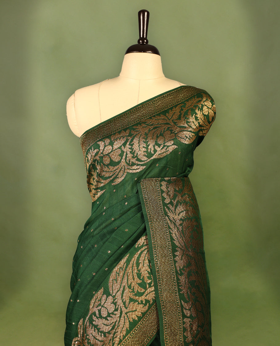 Bottle Green colour Tussar Banaras saree adorned with delicate golden zari motifs on the body, rich floral woven zari border and grand pallu, paired with a matching blouse for an elegant and regal traditional look.