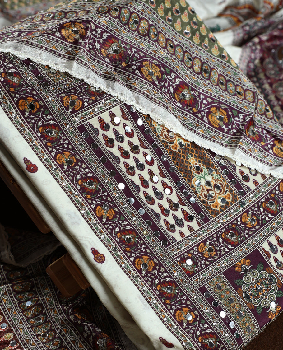 Off white colour churidhar material beautifully detailed with grape colour traditional paisley and floral prints, mirror work highlights, paired with a plain white bottom and a matching printed dupatta with lace border.