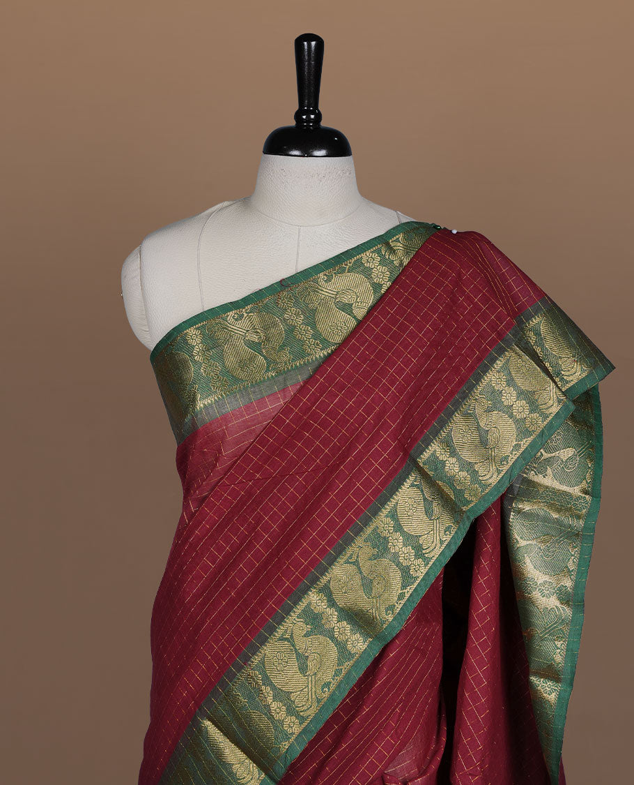 Maroon colour sungudi cotton saree featuring gold zari check pattern across body, contrast green colour with gold zari peacock and floral pattern on border, without blouse piece.