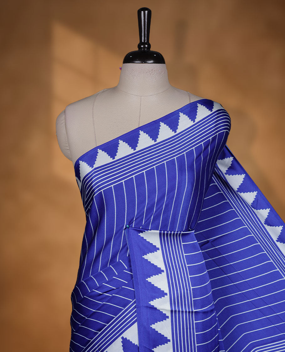 Royal blue colour semi modal saree featuring white colour geometric borders and fine stripe detailing, finished with an oversized circular motif on the pallu, paired with a matching printed blouse.