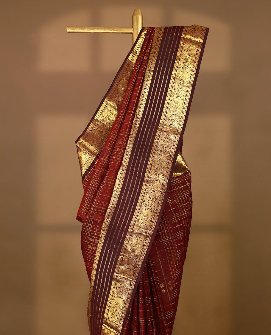 Dark red Colour traditional Kancheepuram silk saree adorned with antique zari check design on the body, featuring a contrasting Traditional border with peacock, deer, and Rudraksham motifs, and paired with a matching blouse.