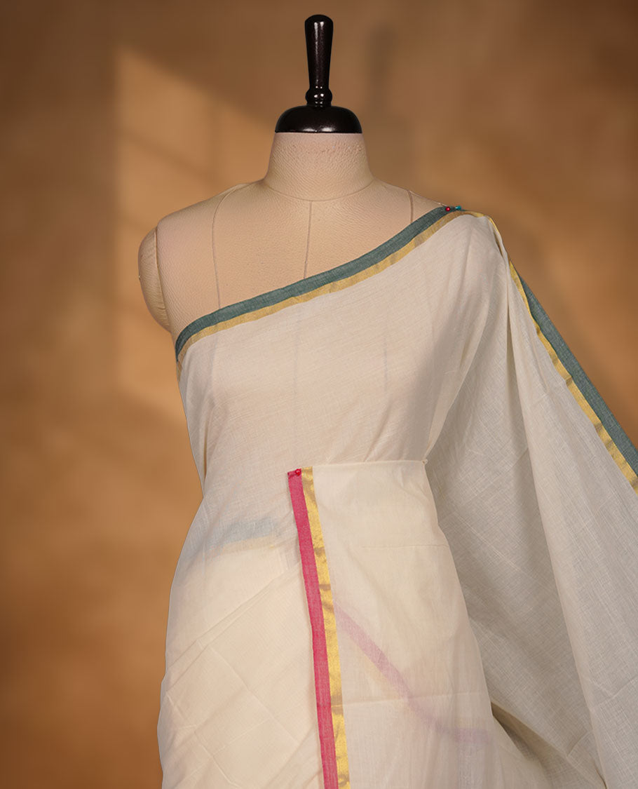Off-white colour cotton Kerala saree featuring a classic gold kasavu border, accentuated with subtle green and pink contrast edging, a plain elegant body, and paired with a matching blouse.