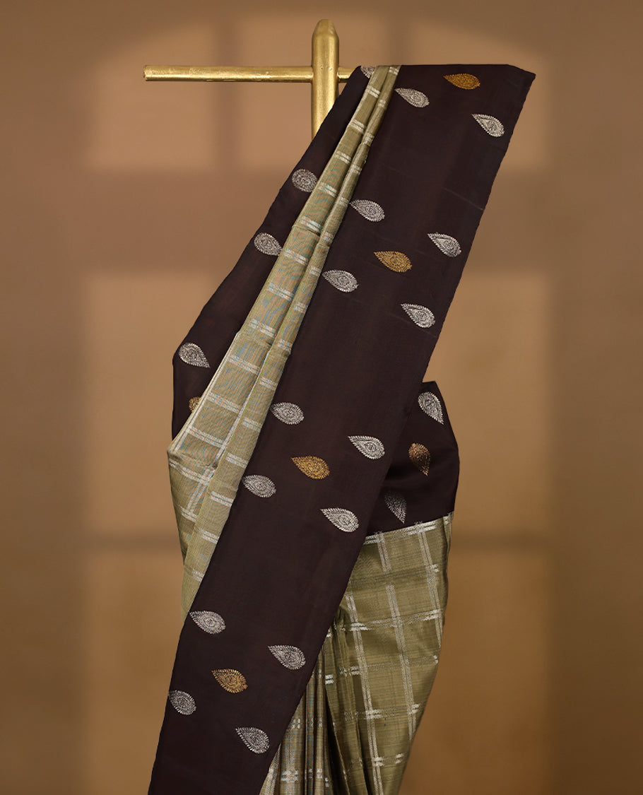 Pastel olive Colour traditional Kancheepuram silk saree adorned with antique check patterns on the body, featuring a deep brown simple border with paisley motifs, and paired with a matching blouse.