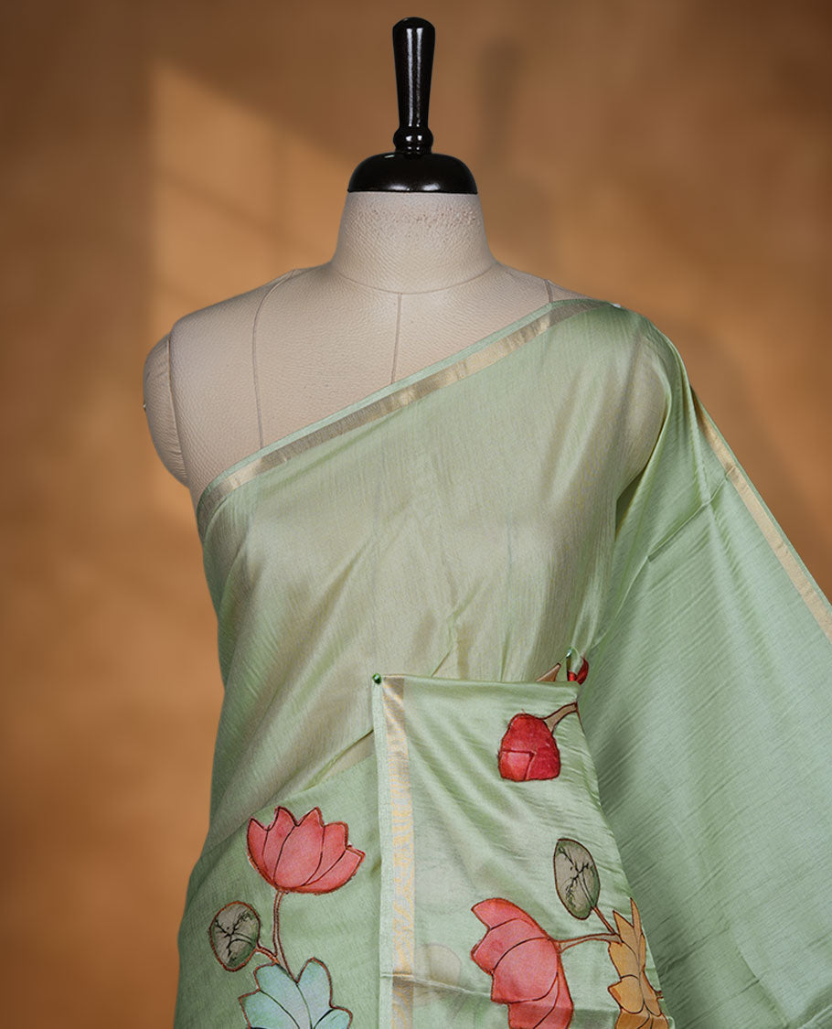 pastel green semi tusser silk saree featuring hand painted floral motifs across the pallu and lower body, highlighted with a subtle zari border and paired with a matching blouse.